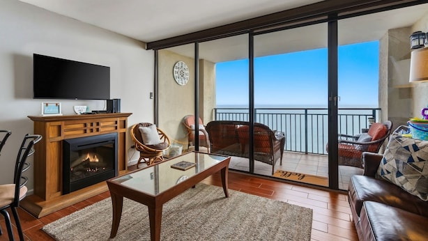 A living room with a fireplace, television, and a balcony with outdoor furniture. - Ocean Forest Plaza 2108 (Myrtle Beach)