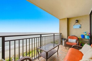 Ein Balkon mit Blick auf den Strand, mit Korbmöbeln, einem Stuhl und einem Regal mit Gegenständen.