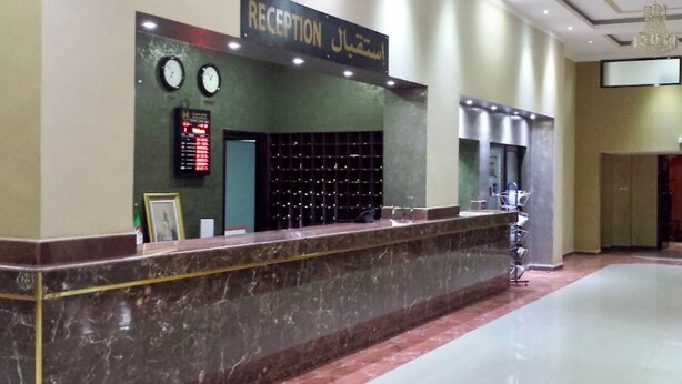 A reception area with a marble counter, clocks, a digital display, and a chandelier. - Le Numidien - Aeroport (Algiers)