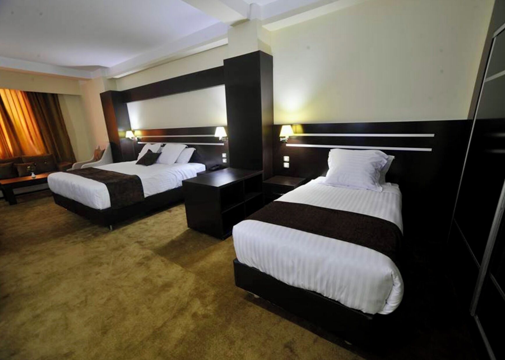 Una habitación de hotel con dos camas, cada una con cabecera, mesitas de noche y lámparas.