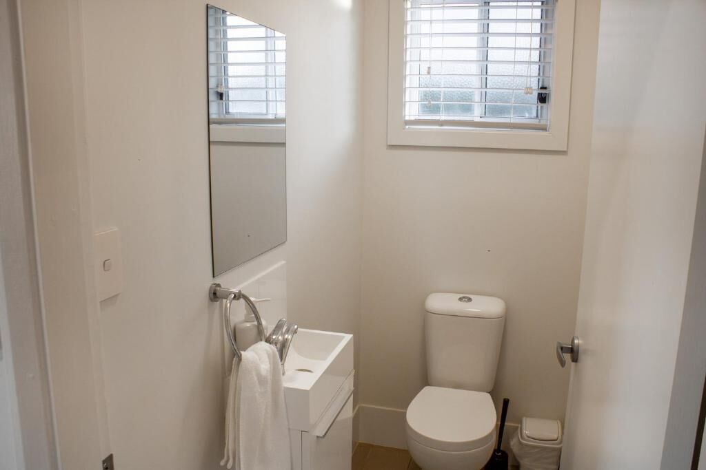Un baño pequeño y blanco con inodoro, lavamanos y un espejo sobre el lavamanos.