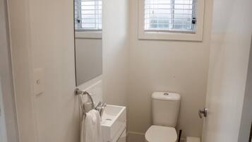 Un baño pequeño y blanco con inodoro, lavamanos y un espejo sobre el lavamanos.