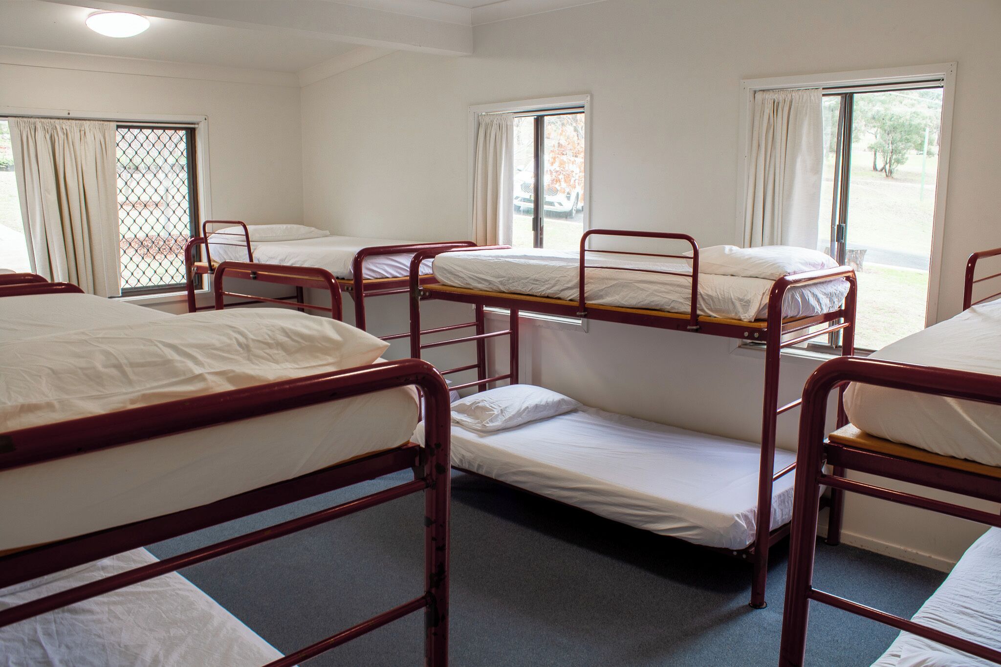 A dormitory room with bunk beds, a window with curtains, and a door with a metal gate.