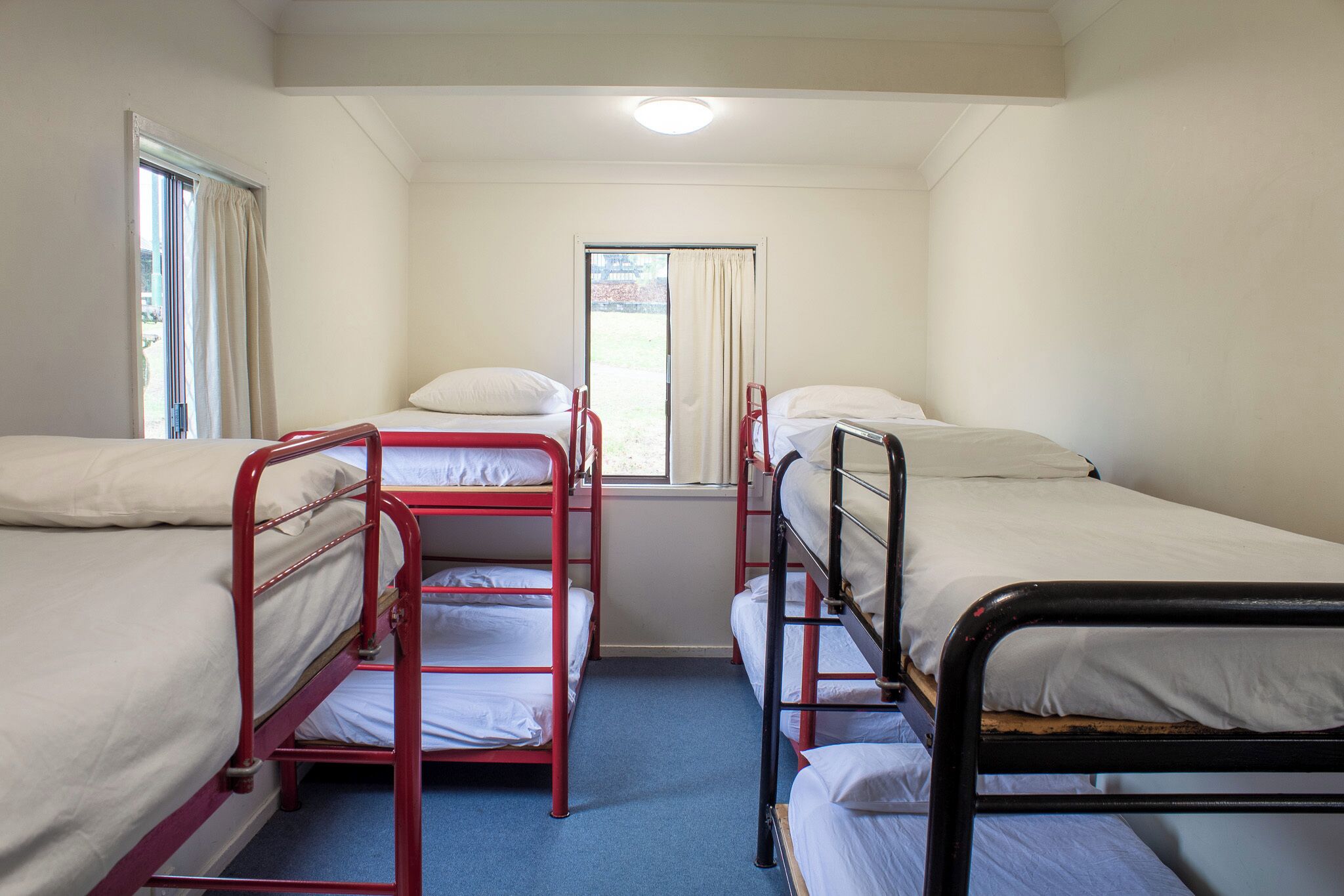 A dormitory room with bunk beds, a window with curtains, and a ceiling light.