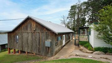 A rustic wooden barn with a metal roof, a small adjacent structure with a green door, and a paved pathway leading to a gated area.