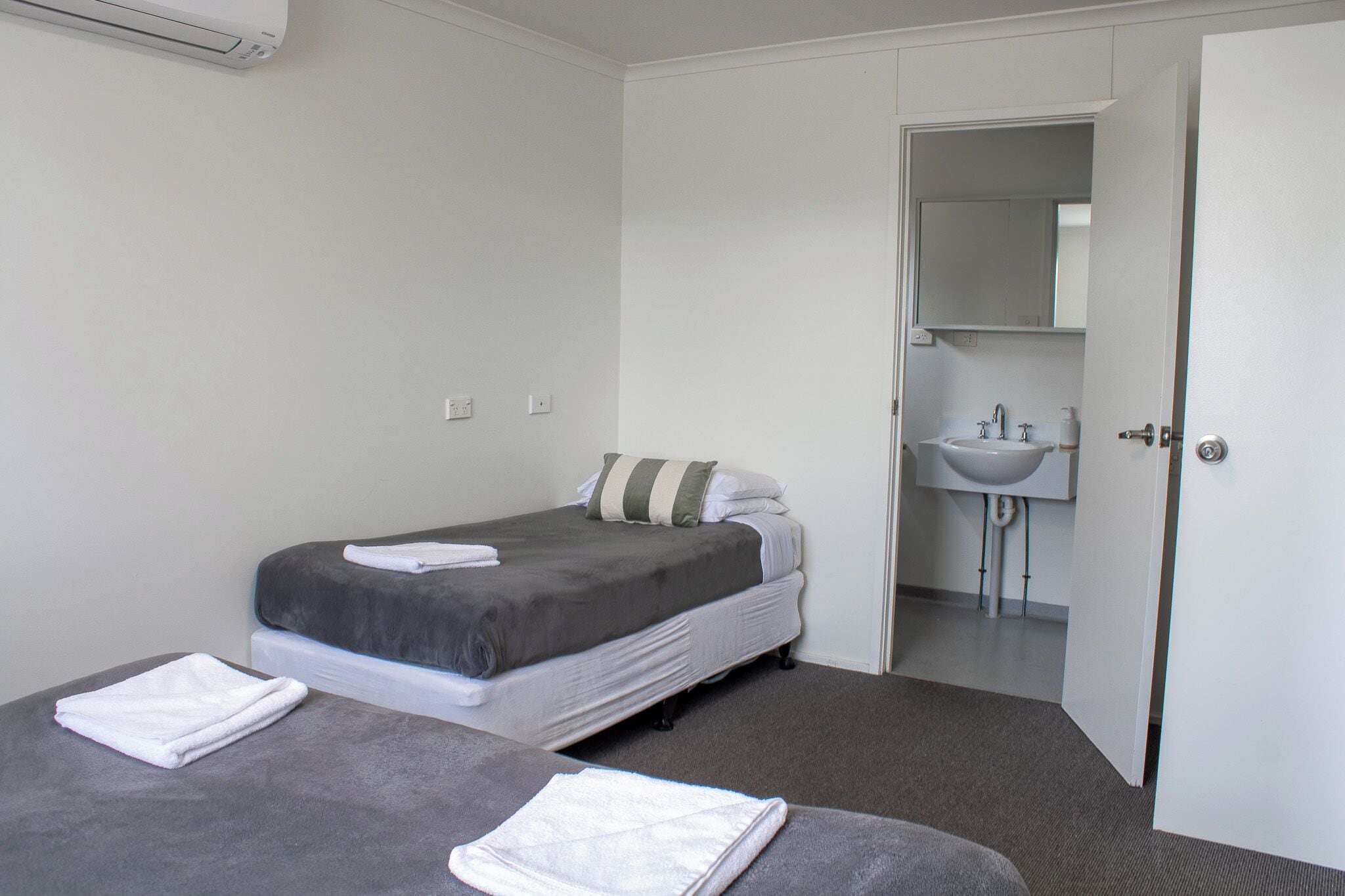 Un dormitorio con dos camas, un baño con lavabo y una puerta que da a otra habitación.