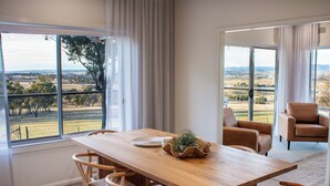 A dining area with a wooden table, chairs, and a view of a rural landscape through large windows.