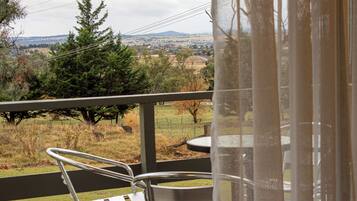 A balcony with a metal chair and table, overlooking a grassy area with trees and a distant town.