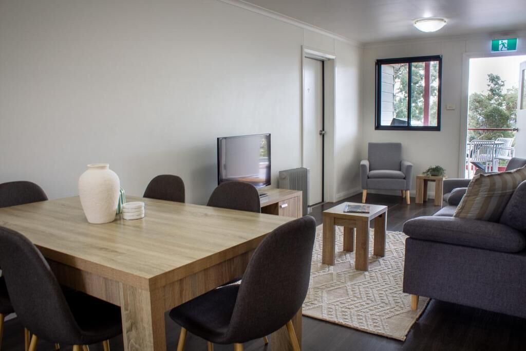 Een moderne woonkamer met een houten eettafel, donkere stoelen, een grijze bank, een televisie en een kleine bijzettafel.