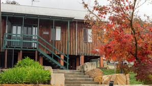 A wooden building with a staircase leading to a porch, surrounded by rocks and plants.