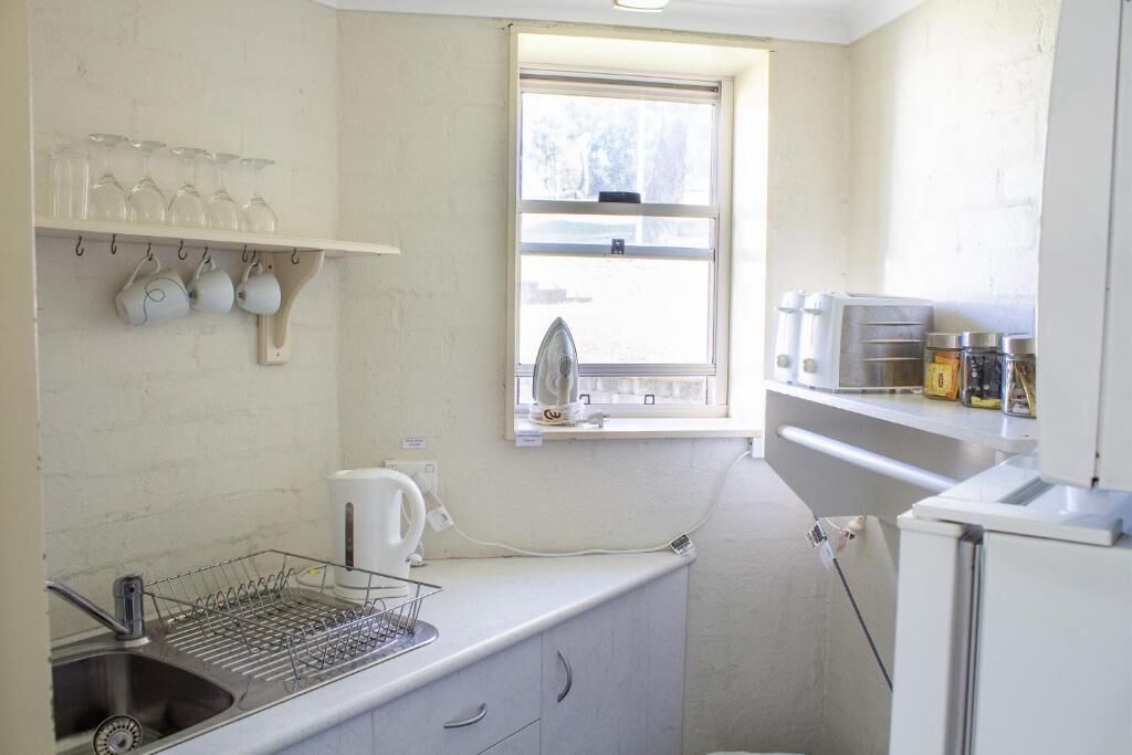 A compact kitchen with a sink, dish rack, and a window.