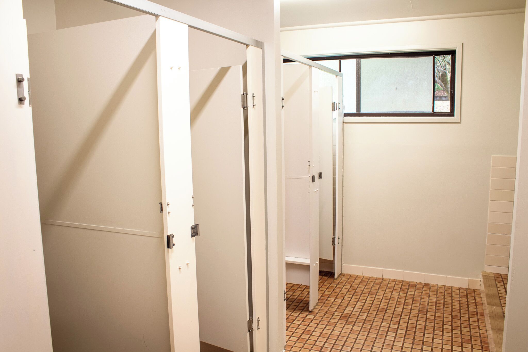 A hallway with white walls, a tiled floor, and a window with a view of trees.