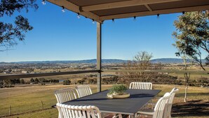 A covered outdoor dining area with a table and chairs, overlooking a scenic landscape.