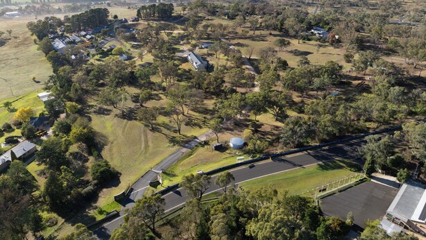 An aerial view of a rural area with scattered houses, a large open field, and a road.