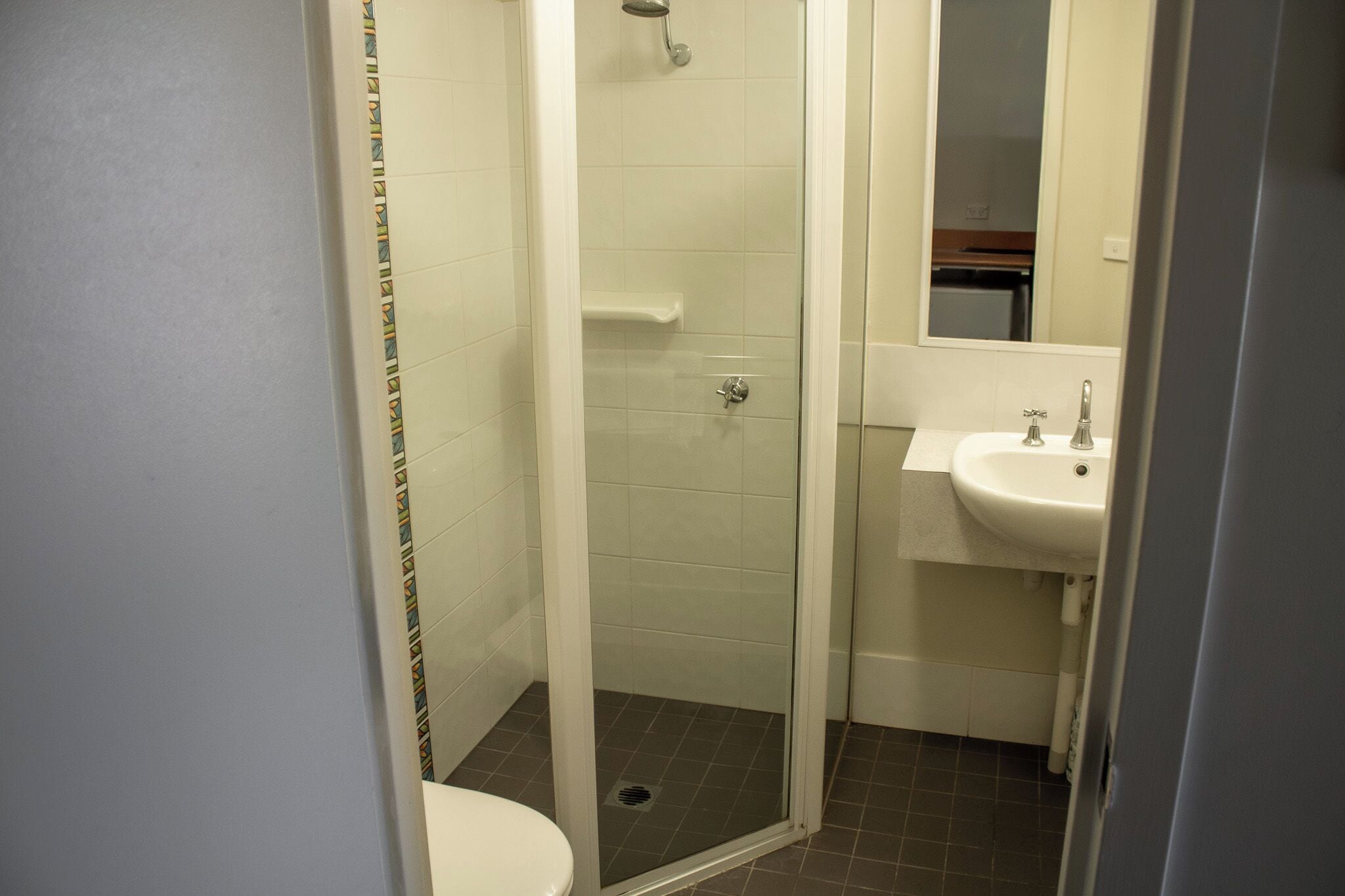 A bathroom with a glass-enclosed shower, a white sink, and a mirror above the sink.