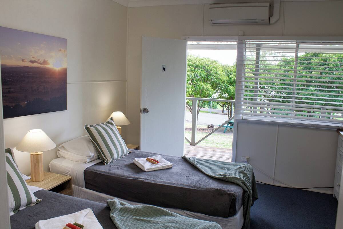 A room with two beds, a painting, a window with blinds, and a door leading to an outdoor area.