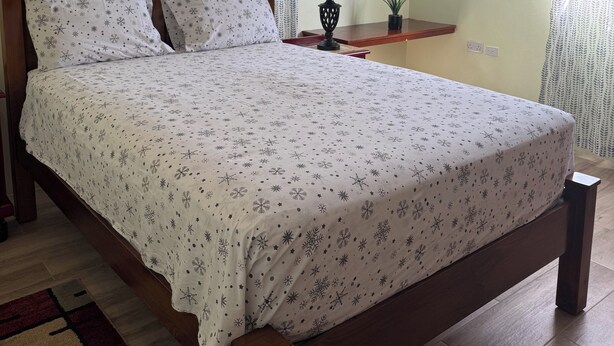 A neatly made bed with a floral bedspread, a bedside table with a lamp, and a small potted plant.