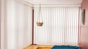 Una habitación con un banco de madera, una cama con ropa de cama color turquesa, una lámpara sobre una mesita de noche de madera y una cesta colgante.