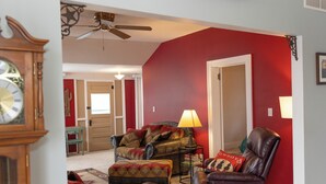 Una sala de estar con una pared roja, un ventilador de techo, un reloj y un sillón de cuero.