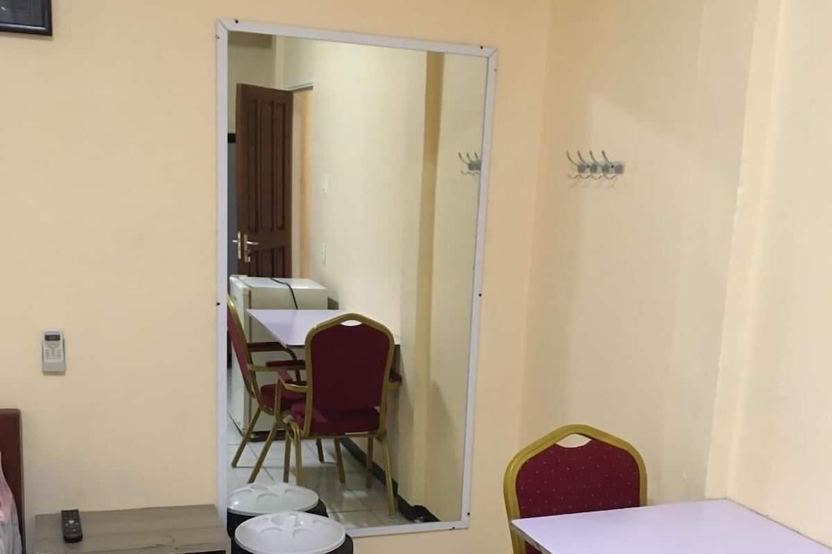 A small, clean room with a single table and two chairs, a mirror, a trash bin, and a small cabinet.