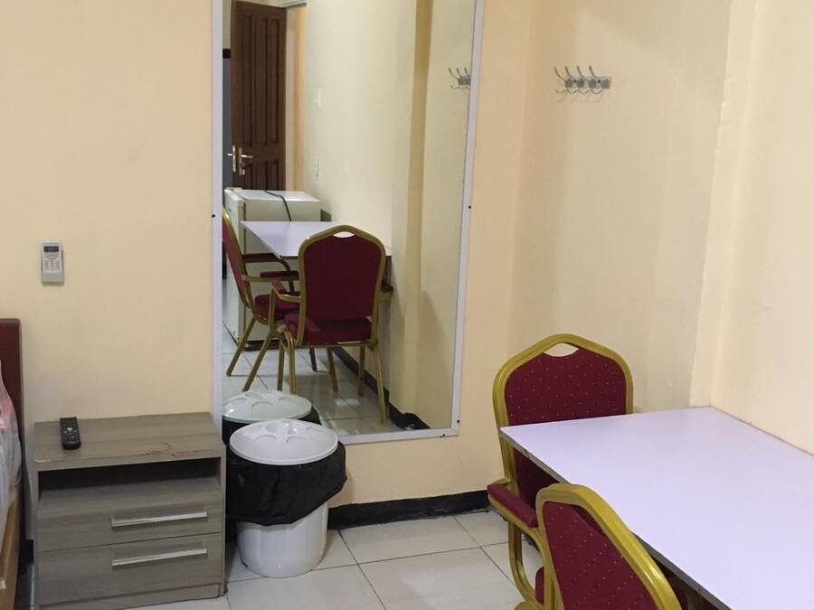 A small, clean room with a single table and two chairs, a mirror, a trash bin, and a small cabinet.