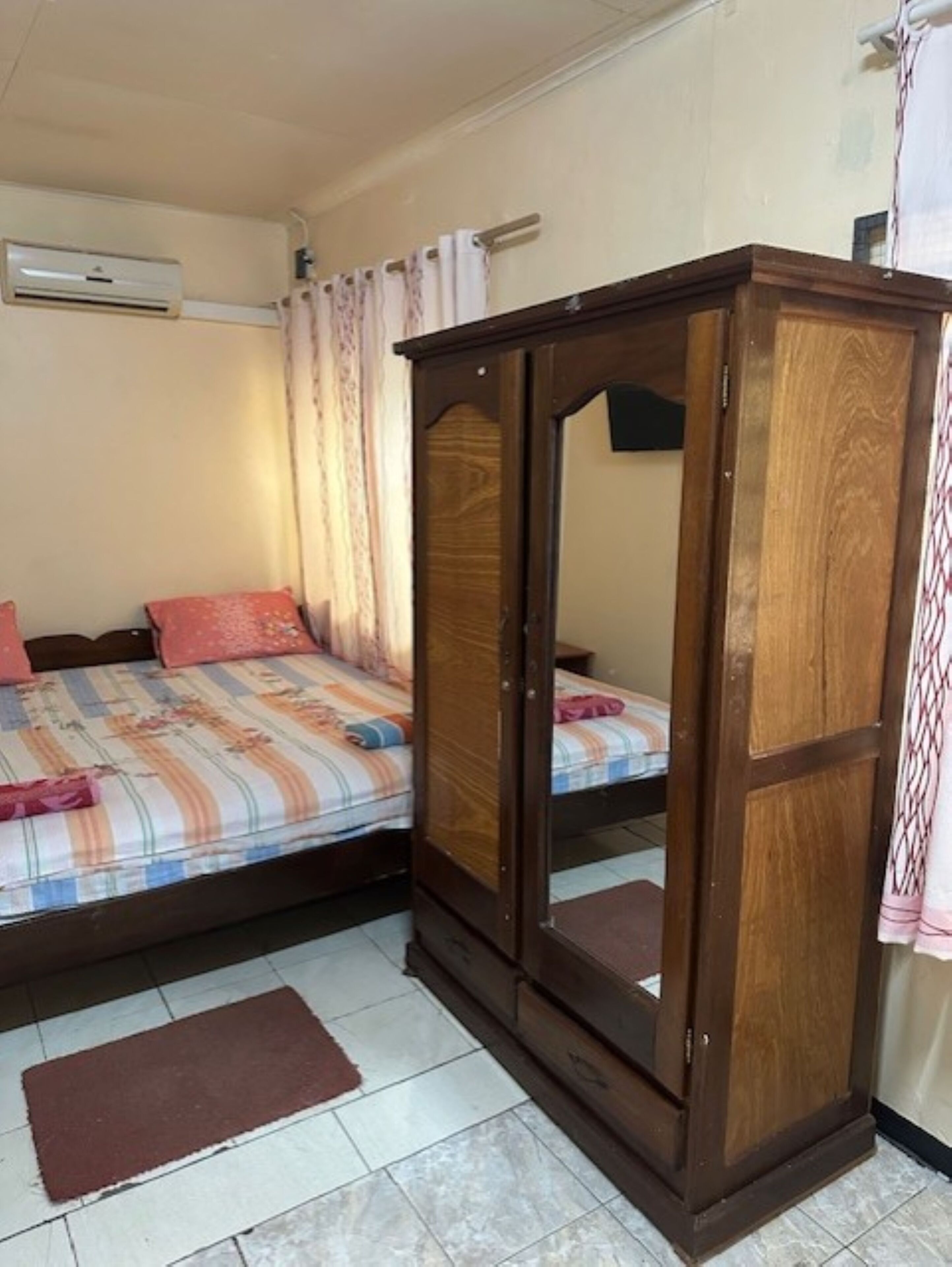Quarto com duas camas, um guarda-roupa de madeira e um aparelho de ar condicionado na parede.