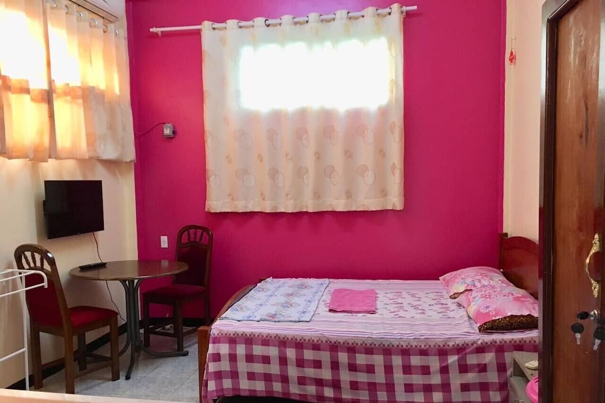 A bedroom with a bed, a chair, a small table, and a television.