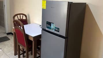 A compact kitchen with a refrigerator, a dining table, and two chairs.
