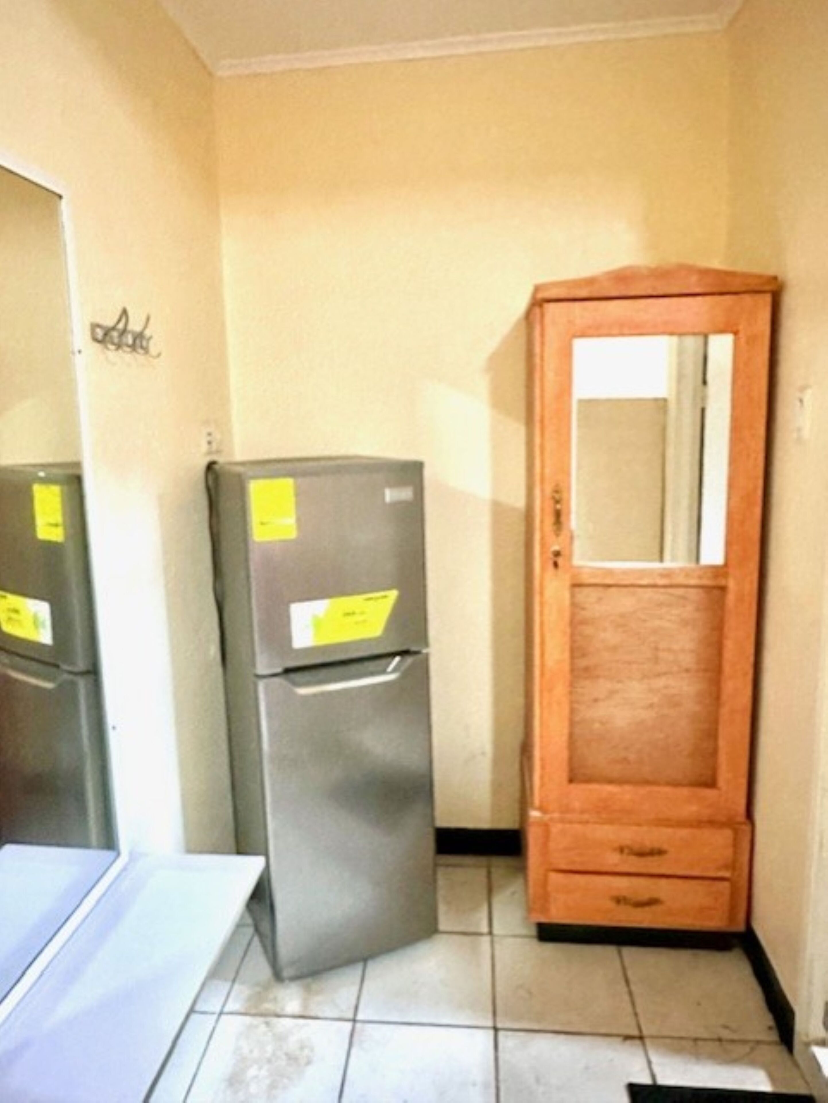 Una habitación pequeña con un armario de madera, un refrigerador gris y una mesa blanca.