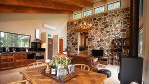 A spacious living area with a stone wall, a fireplace, and a dining table set with chairs. - Bruny Island Haven - The Studio (Adventure Bay)
