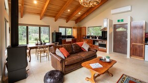 A spacious living area with a wooden ceiling, a fireplace, a sofa, a coffee table, and a view of the outdoors. - Bruny Island Haven - The Studio (Adventure Bay)