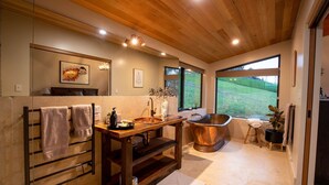 A modern bathroom with a wooden vanity, a freestanding bathtub, and a large window offering a view of a green landscape. - Bruny Island Haven - The Studio (Adventure Bay)