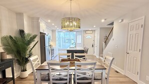 Un comedor con candelabro, sillas blancas, mesa de madera y una planta en maceta.
