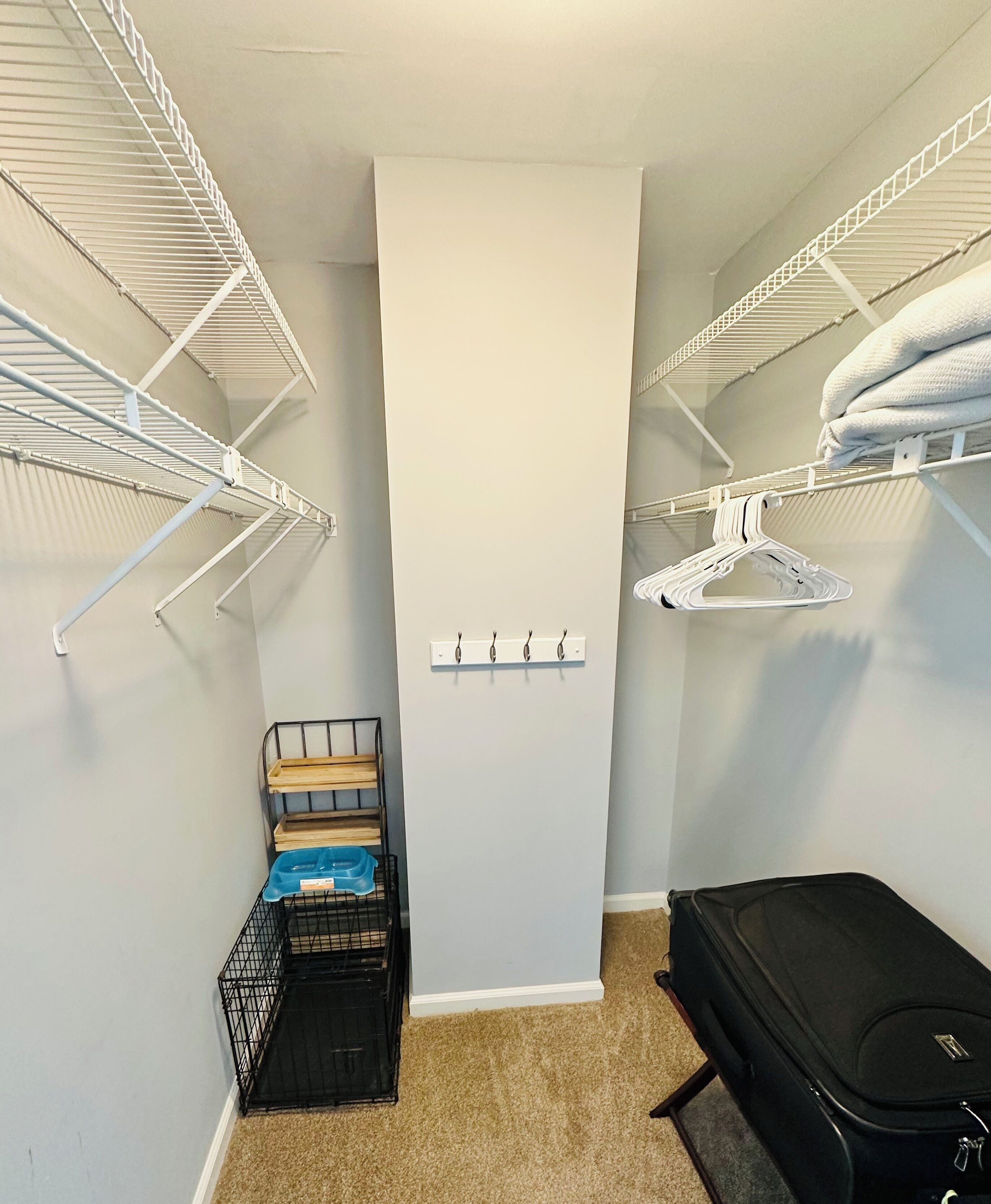 Un dressing accessible sans porte, avec des étagères en métal, un banc en bois et une valise noire.