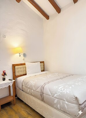 A bedroom with a bed, a nightstand, a lamp, and a small table with a vase of flowers. - Natys guest house (Cusco)