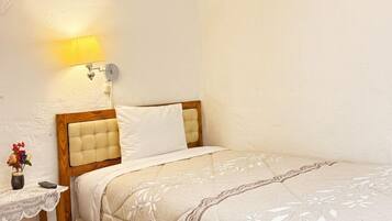 Un dormitorio con cabecera de madera, una mesita de noche con lámpara, un pequeño jarrón con flores y una cama con colcha estampada.