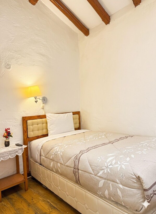 A bedroom with a wooden headboard, a bedside table with a lamp, a small vase with flowers, and a bed with a floral-patterned bedspread. - Natys guest house (Cusco)