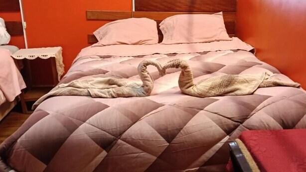 A hotel room with a large bed, a bedside table, and a red chair. - Natys guest house (Cusco)