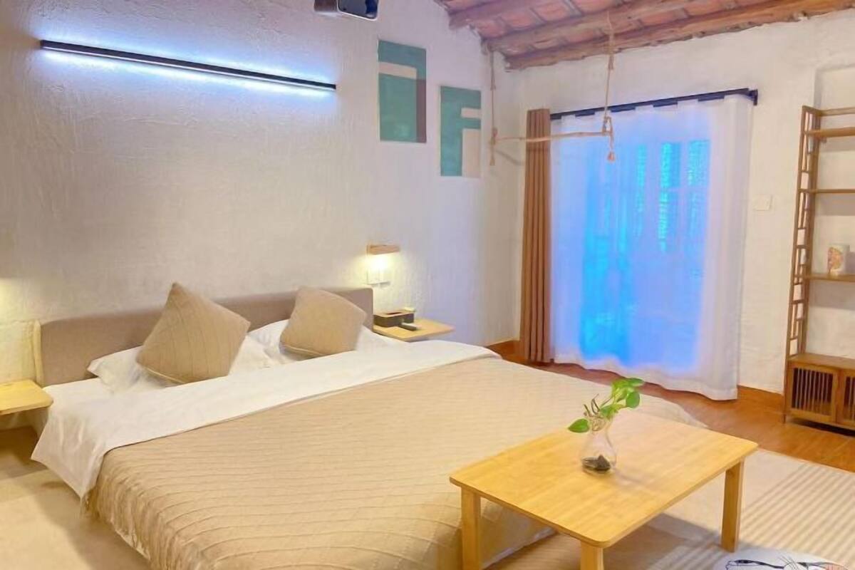 A bedroom with a bed, bedside tables, a nightstand, a wooden table, and a window with curtains.