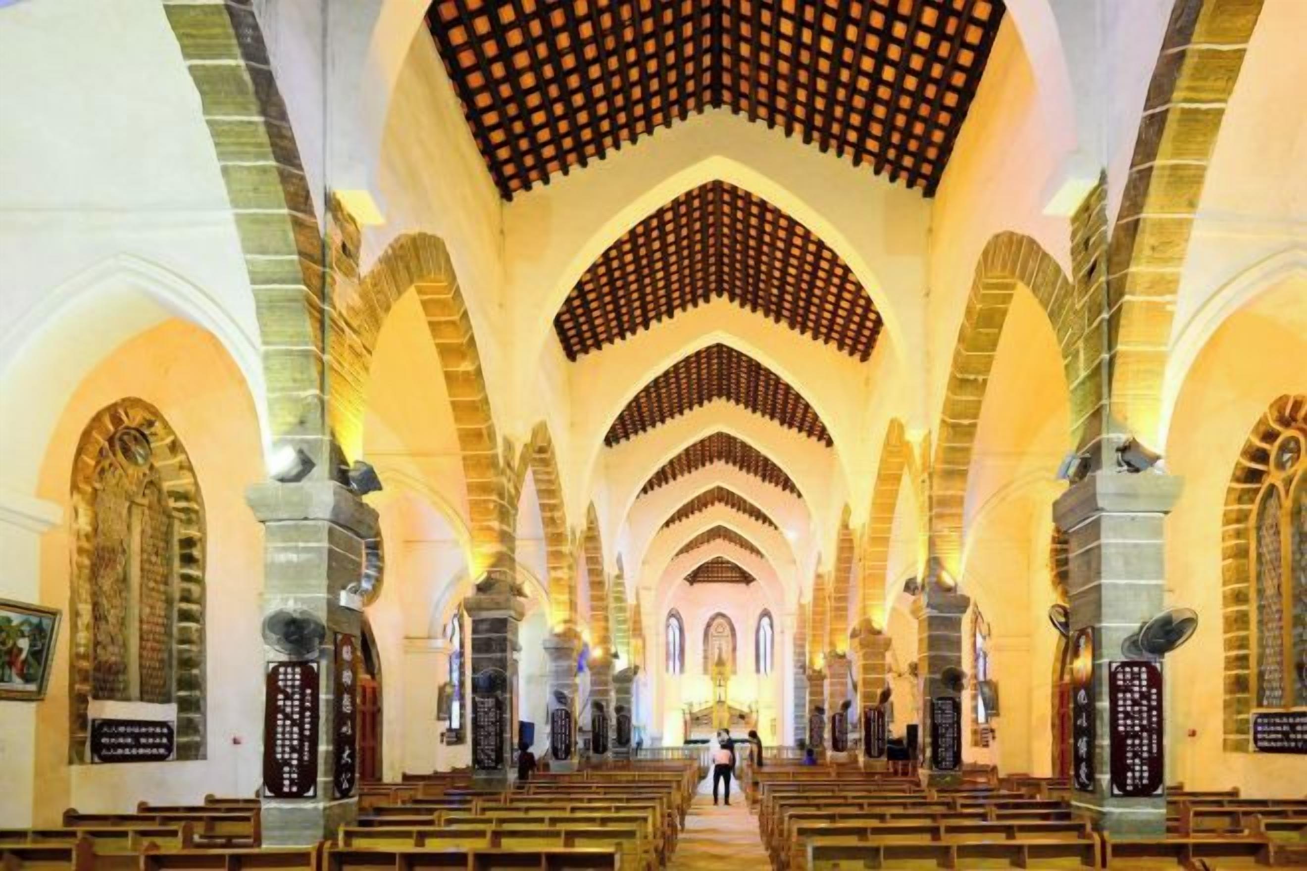 Ein Kircheninneres mit hohen Gewölbedecken, Reihen von Kirchenbänken und Steinsäulen.