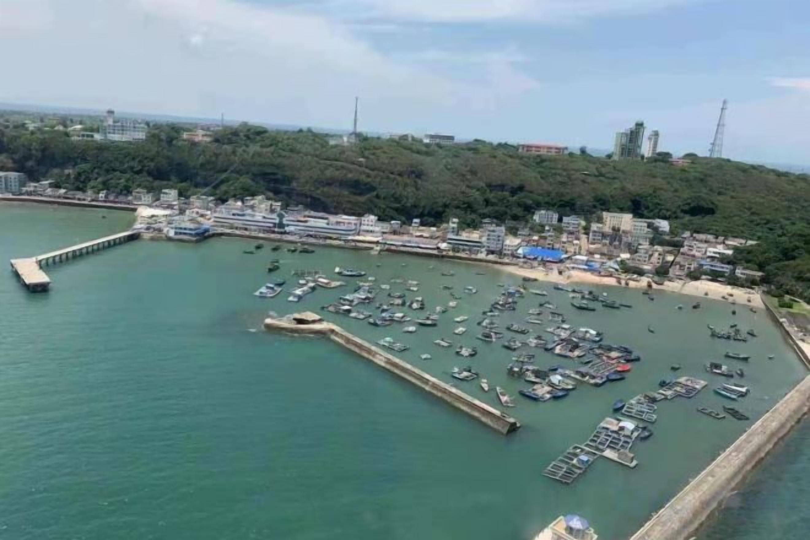 Un port de plaisance situé sur la côte, avec des bateaux amarrés, une jetée et des bâtiments en arrière-plan.