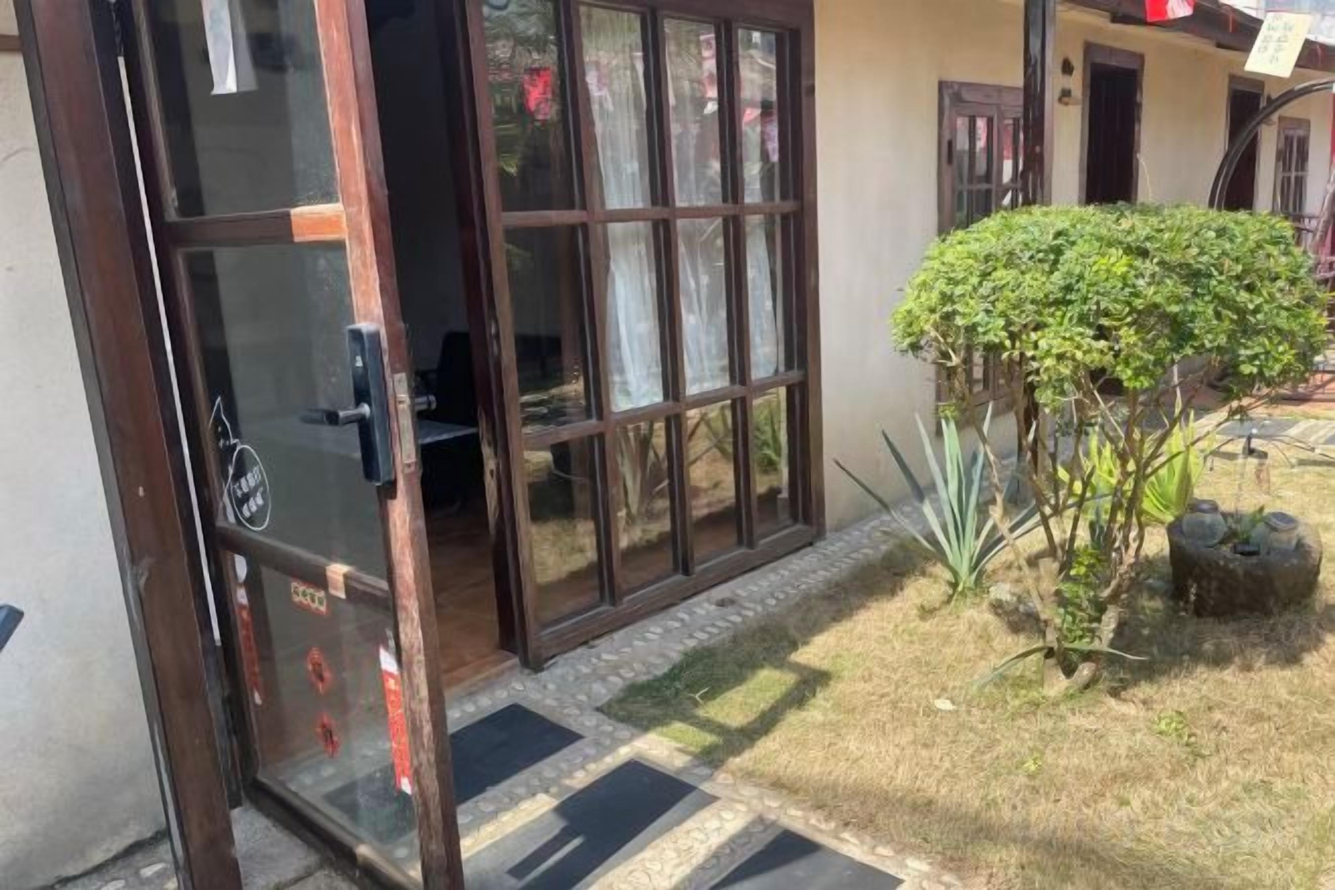 A residential property with a sliding glass door entrance, a small garden with a shrub, and a tiled pathway.