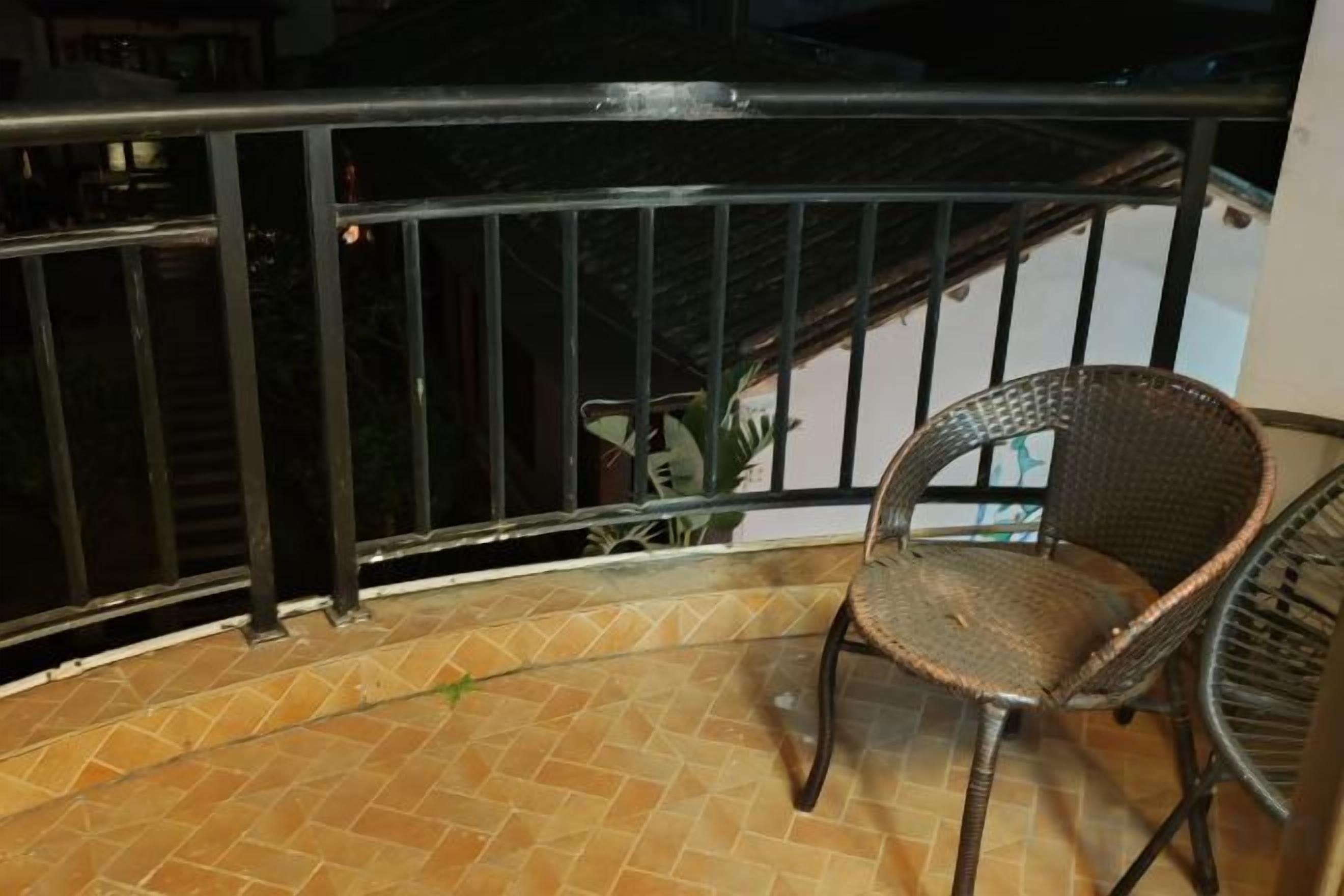 A balcony with a wicker chair, a metal railing, and a tiled floor.