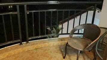 A balcony with a wicker chair, a metal railing, and a tiled floor.