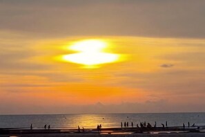 Un atardecer sobre una playa con gente y un muelle.