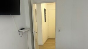 Une chambre à coucher avec un grand lit, un téléviseur fixé au mur, une table de chevet et une porte donnant sur une autre pièce.