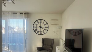 Un salon avec une grande horloge murale, un téléviseur à écran plat, un fauteuil gris et une vitrine.