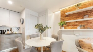 Una cocina moderna con gabinetes blancos, una mesa redonda con sillas y una pared de ladrillo decorativa con estantes.