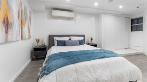 Un dormitorio moderno con una cama grande, una mesita de noche con lámpara y aire acondicionado instalado en la pared.