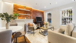 Una sala de estar moderna con una pared de ladrillo decorativa, una chimenea, un televisor de pantalla plana y un comedor con mesa y sillas.